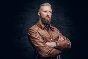 stylish blond bearded male with crossed arms dressed in a brown leather pilot jacketasa